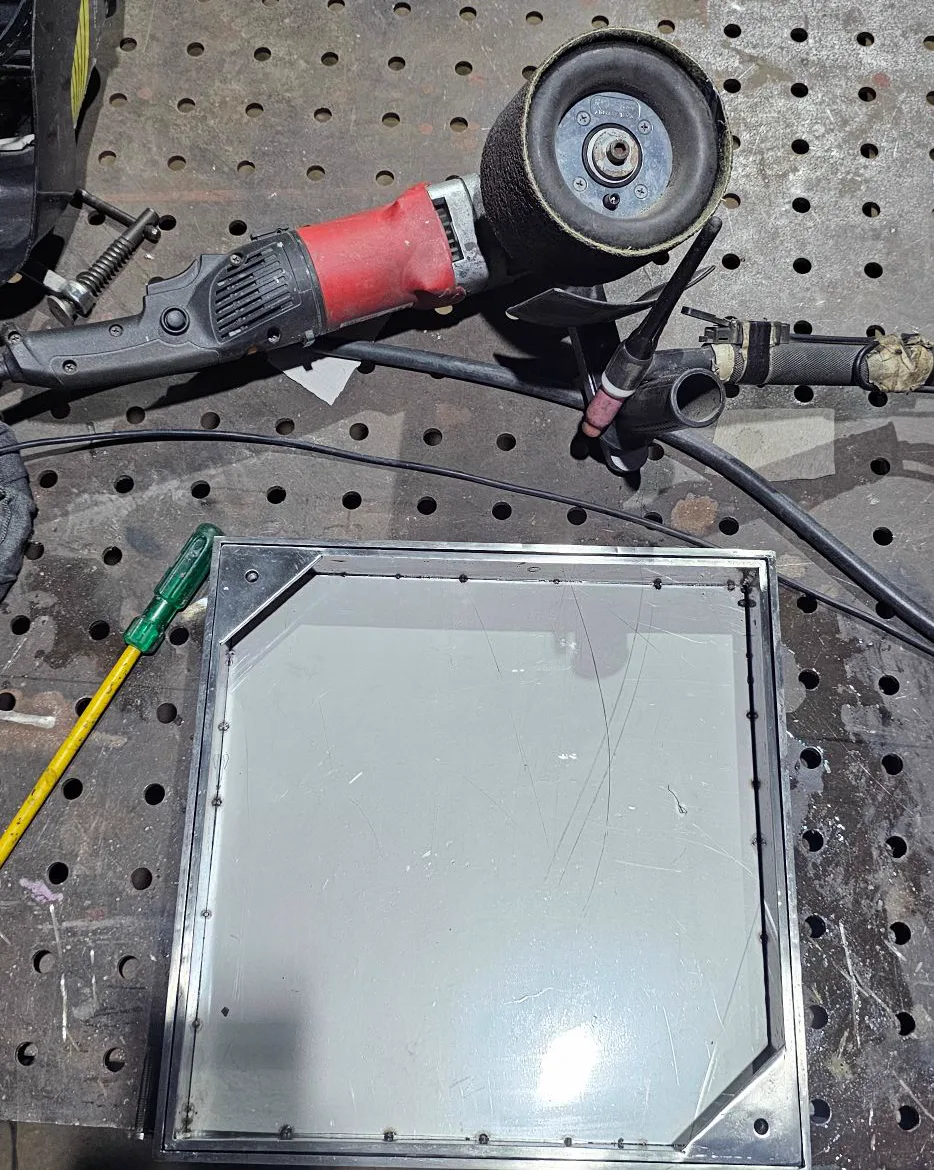 Satin finishing machine next to a stainless steel chamber cover tray